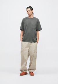 Szürke pamut póló mellzsebbel, laza bézs színű cargo nadrág oldalzsebekkel, narancssárga texturált talpú cipővel párosítva.