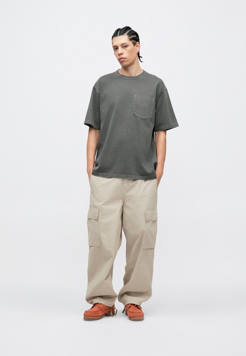 Grå bomulls-t-shirt med bröstficka, kombinerad med lösa beige cargobyxor med sidofickor och orangea skor med texturerad sula.