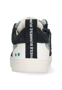 Sneaker blanc et bleu marine avec un dos texturé, doté d'une languette bleu foncé et d'accents de point vert sur le talon.