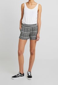 Černobílé vzorované šortky s elastickým pasem a postranními kapsami, spárované s bílým tílkem a černými teniskami.
