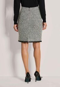 Grauer Tweed-Bleistiftrock mit Fransen-Saum, ausgestattet mit einem Reißverschluss hinten. Kombiniert mit schwarzen High Heels, die eine strukturierte Oberfläche zeigen.