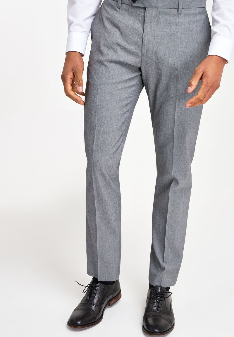 Pantalons tailleur gris avec une texture subtile, taille plate et jambes droites, associés à des chaussures de ville en cuir noir.