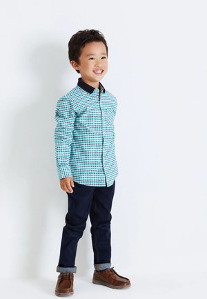 Langsleeve geruit overhemd in turquoise, groen en rood; donkere kraag; gecombineerd met donkere spijkerbroek en bruine schoenen met opgerolde cuffs.