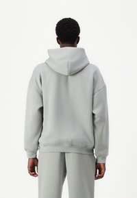 Grå hættetrøje med afslappet pasform, med stor hætte, ribkant ved ærmer og nederkant. Lavet af blødt stof, vist bagfra.