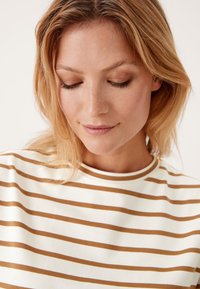 Gestreepte top met horizontale lijnen in beige en lichtbruin. Zachte stof, ronde halslijn en korte mouwen.