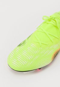 Bright neon yellow soccer shoe with textured mesh upper, intricate white pattern, and black sole with pink accents. Laces are fitted in place.