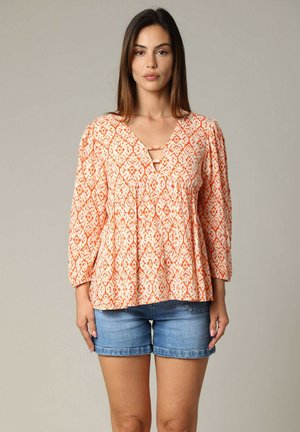 Blouse à motifs orange avec un décolleté en V, des manches trois-quarts et un design plissé, associée à un short en denim. Tissu léger avec une finition texturée.