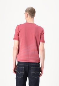 Støvet rose t-skjorte med korte ermer og rund hals, med kontrasterende synlige sømmer, sammen med mørke jeans med baklommer.