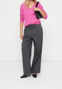 Maglione rosa a scollo a V e maniche lunghe abbinato a pantaloni grigi a gamba larga e décolleté nere con punta appuntita, con una borsa nera testurizzata.