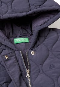 Námořnický prošívaný kabát s kapucí, stříbrným zipem, patentkami a zelenou značkovou etiketou uvnitř. Hladká textura s polstrovaným prošíváním.