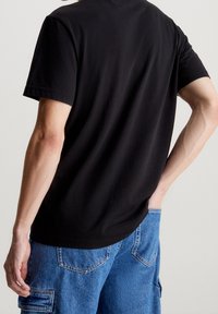 Černé bavlněné tričko s krátkým rukávem, volný střih a zakulacený lem, nošené s světle modrými denimovými cargo šortkami.