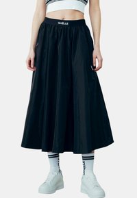 Gonna nera fino al ginocchio realizzata in materiale leggero con vita elasticizzata. Abbinata a sneaker bianche e calze a righe.