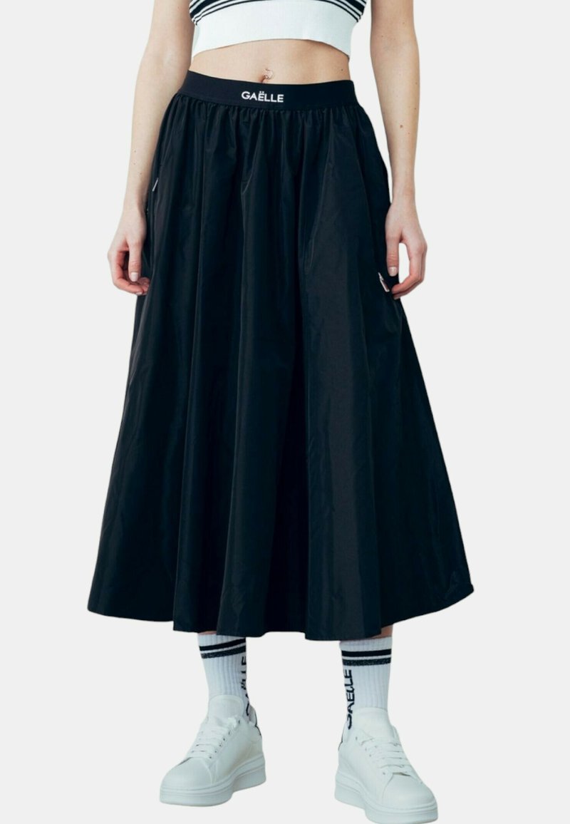 Gonna nera fino al ginocchio realizzata in materiale leggero con vita elasticizzata. Abbinata a sneaker bianche e calze a righe.