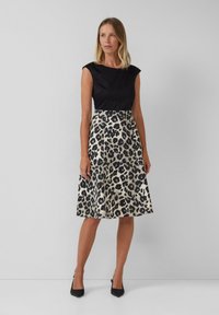 Top noir ajusté avec des manches courtes, associé à une jupe jusqu'au genou avec un imprimé léopard beige et noir. Porté avec des talons noirs.