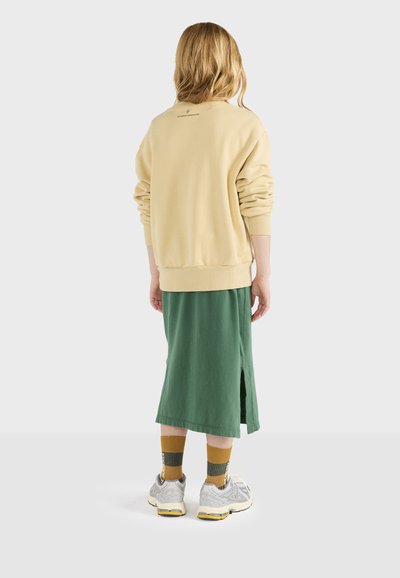 Lys beige oversized sweatshirt med ribbede manchetter, parret med en lang grøn nederdel med en side-slids. Grå sneakers og mønstrede sokker.