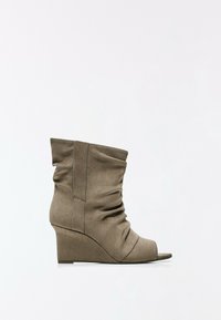 Bottine taupe en daim à bout ouvert, avec un talon compensé de hauteur moyenne et des détails froncés sur la tige, sur fond blanc.