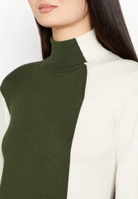 Sweter z golfem o wzorze w blokach kolorów, z oliwkowozielonymi i kremowymi sekcjami, wykonany z miękkiego materiału o prążkowanej teksturze.
