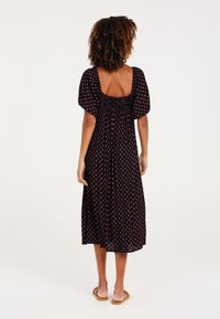 Svart midiklänning med korta puffärmar, smockad rygg och rosa diamantmönster. Lätt tyg och avslappnad passform för enkel rörelse.