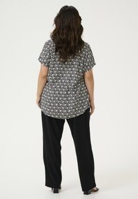 Blouse à manches courtes à motifs noir et blanc avec un ourlet arrondi, associée à un pantalon noir ample et des chaussures noires à bout ouvert.