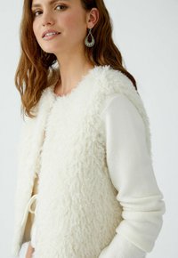 Witte nepbont vest met een gestructureerd oppervlak, open voorkant, gecombineerd met een aansluitend wit longsleeve shirt. Kenmerkt zich door de zachte, gezellige stof.
