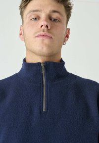 Dunkelblauer Fleece-Pullover mit hohem Kragen und Reißverschluss. Weiche Textur mit dezentem Glanz und minimalen Nähdetails.