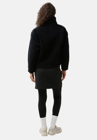Black plush fleece pullover with a high collar, paired with a black skirt and black leggings. Features visible labels and a textured surface.