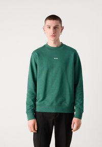 Sudadera verde con cuello redondo, puños y dobladillo acanalados; presenta un pequeño logo blanco de "BOSS" en el pecho. Tejido de mezcla de algodón suave.