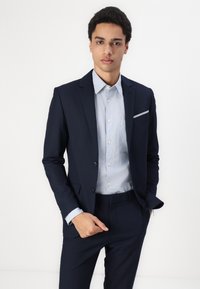 Navy suit with a fitted design, featuring a single-breasted jacket, notch lapels, and a light blue button-up shirt underneath.