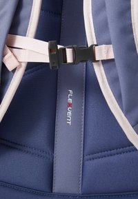 Interiér batohu so námorníckou modrou látkou a svetloružovými popruhmi. Obsahuje čierne spona a biele označenie "FLEXVENT".