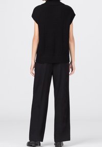 Svart stickad topp med hög krage och ribbad textur, i kombination med löst sittande svarta byxor och svarta ankelstövlar.