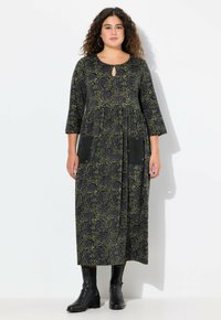 Černé dlouhé šaty s zeleným vzorem růží, kulatým výstřihem, detailem ve tvaru klíče, třičtvrtečními rukávy a dvěma předními kapsami. Nosené s černými kotníkovými botami.