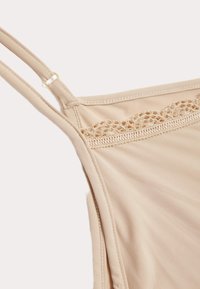 Canotta beige con spalline regolabili, dotata di un delicato pizzo lungo lo scollo e tessuto morbido e elasticizzato. Cuciture piatte per il massimo comfort.