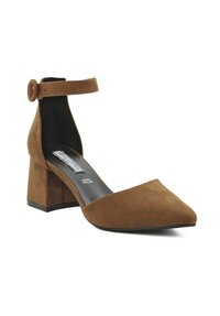 Pump in suede marrone con tacco a blocco, punta affusolata e cinturino alla caviglia dotato di una fibbia rotonda. All'interno presenta una soletta nera con il marchio.