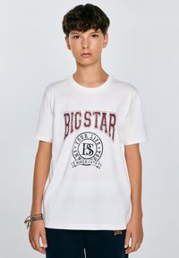 Valge puuvillane T-särk, millel on suur "BIG STAR" trükk burgundia ja musta ringikujulise logoga koos tekstiga. Ümar kaelus ja lühikesed varrukad.