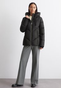 Giacca a vento nera con cappuccio, dotata di chiusura con zip e motivo a rombi. Abbinata a pantaloni grigi a vita alta e scarpe nere.