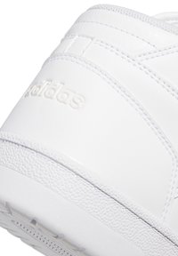 Zbliżenie na tylną część białego obuwia Adidas, ukazujące wytłoczone logo oraz szczegóły teksturowanej podeszwy.