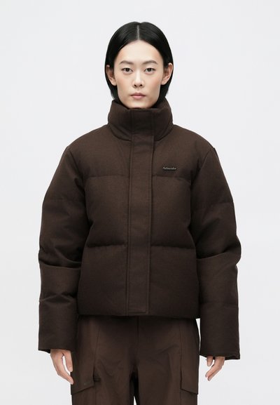 Giacca corta marrone in stile puffer con colletto alto, dotata di sezioni trapuntate e un logo discreto sul petto. Realizzata in tessuto testurizzato.