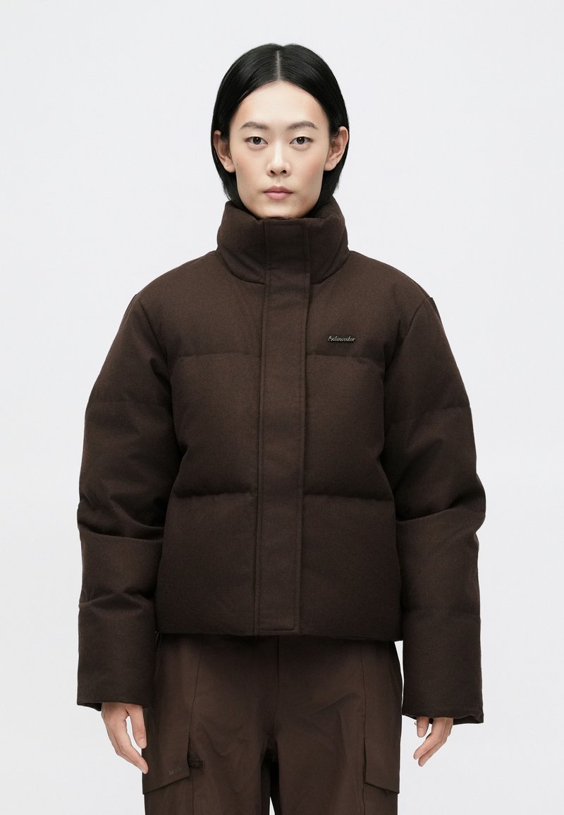 Veste courte en duvet marron avec col montant, présentant des sections matelassées et un logo discret sur la poitrine. Fabriquée en tissu texturé.