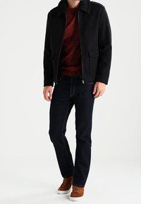 Svart jacka med pälskrage, röd tröja under, mörk denimjeans och bruna skor. Enkelt design med dragkedjestängning och fickor.