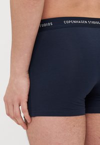 Sötétkék pamut elasztikus boxer alsó, puha derékpánttal, amelyen fehér betűkkel szerepel a "Copenhagen Studios" felirat. Simaság, testhezálló kialakítás.