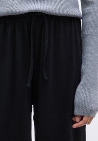 Γκρι ριγωτό πουλόβερ με μακριά μανίκια και φαρδιά μαύρη ζώνη με κορδόνι. Το ύφασμα φαίνεται μαλακό με λεία υφή.