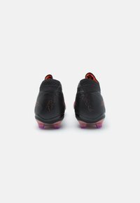 Black soccer boots with a textured finish, featuring red accents and a low collar. Clear, purple-tinted studs provide traction.
