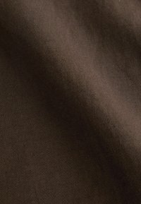 Gros plan d’un tissu lisse marron foncé avec une texture subtile de tissage diagonal et des plis doux créant des ombres délicates.