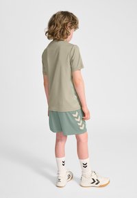 Ljus olivgr�ön kortärmad skjorta, ljusblå shorts med krämfärgat chevronmönster, vita strumpor med svarta detaljer och vita sportskor.