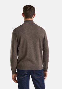 Maglione di lana marrone con colletto alto, polsini e orlo a costine. La parte posteriore presenta una finitura liscia e testurizzata, abbinato a jeans in denim scuri.