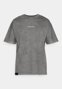 Γκρίζο βαμβακερό μπλουζάκι με στρογγυλή λαιμόκοψη, κοντά μανίκια και μια διακριτική λογότυπο σε λευκό στο στήθος. Το ύφασμα έχει μαλακή, φθαρμένη υφή.