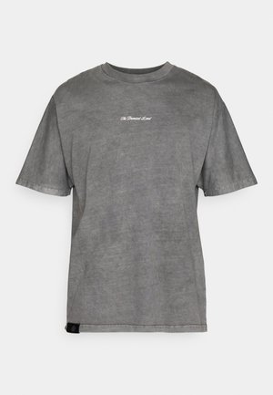 Maglietta in cotone grigia con collo rotondo, maniche corte e un logo bianco discreto sul petto. Il tessuto ha una consistenza morbida e usurata.