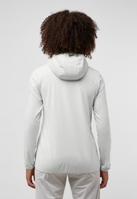 Witte lichte hoodie met een getailleerd ontwerp, lange mouwen en een verstelbare capuchon. Gladde stoftextuur, zonder zichtbare merknaam of patronen.