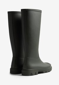 Bottes de pluie en caoutchouc vert foncé, hautes, avec une surface lisse, un bord texturé en haut et une semelle robuste et épaisse pour une bonne adhérence.
