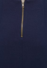 Veste zippée navy avec un zip en métal doré, texture de tissu lisse et lignes épurées, soulignant un design minimaliste.